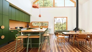 Une cuisine moderne avec des meubles de couleur verte, un îlot central en bois et des tabourets de bar.