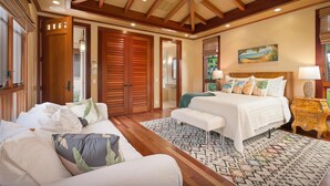 A spacious bedroom with a large bed, a sitting area, and a ceiling fan. - Maile Hale-Serenity Home (Waimea)