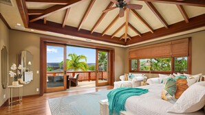 A spacious bedroom with a large bed, a ceiling fan, and a view of palm trees through the sliding glass door. - Maile Hale-Serenity Home (Waimea)