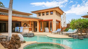 A pool area with lounge chairs, a hot tub, and a building with a tiled roof. - Maile Hale-Serenity Home (Waimea)