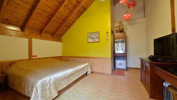 A bedroom with a bed, wooden ceiling, a yellow wall, a television, and a shelf with items. - Shin Ming Shan (Nantou)