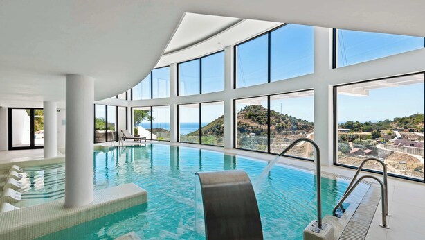 A modern indoor swimming pool with large windows offering views of a coastal landscape. - Palo Alto 6 | Marbella Panoramic Views Luxury (Málaga)