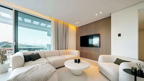 A modern living room with a sectional sofa, a round coffee table, and a flat-screen TV mounted on the wall. - Palo Alto 6 | Marbella Panoramic Views Luxury (Málaga)