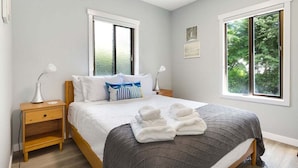 Une chambre à coucher avec un lit, deux tables de chevet, une fenêtre et une vue sur la verdure.