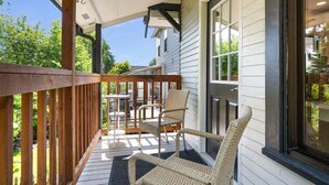Une véranda couverte avec une balustrade en bois, des chaises en osier et une petite table.