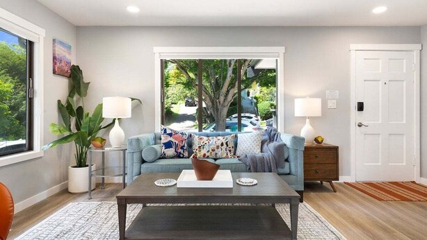 Un salon avec un canapé, une table basse et une table d’appoint. Il y a une fenêtre donnant sur des arbres et on peut voir une voiture à l’extérieur.