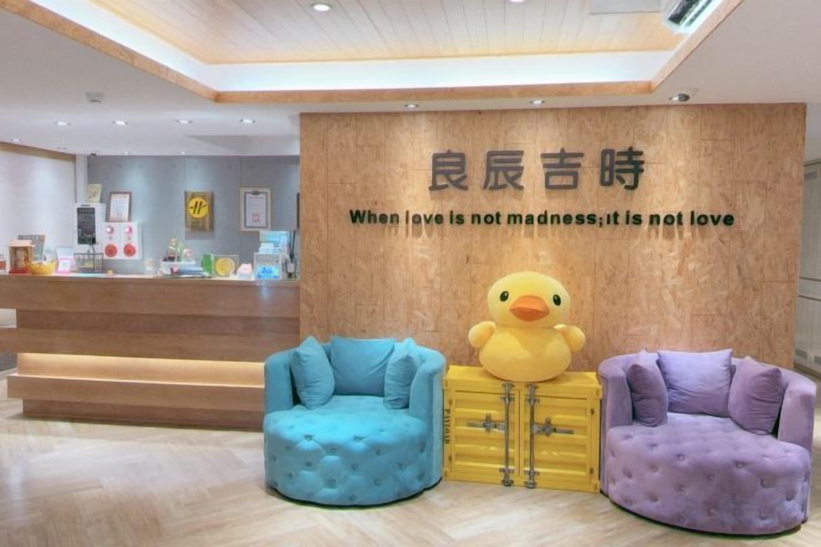 A reception area with a wooden wall, a large duck sculpture, and two plush chairs.
