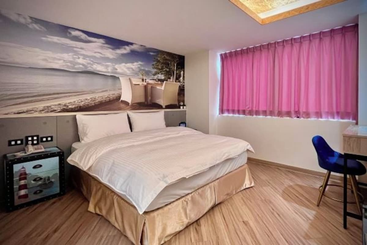 A bedroom with a bed, a desk, a chair, a window with curtains, and a wall mural.