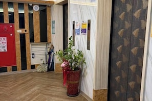 Un espace d’accueil doté d’un plancher en bois, d’un détecteur d’incendie rouge, d’une plante en pot et d’un mur orné de motifs.