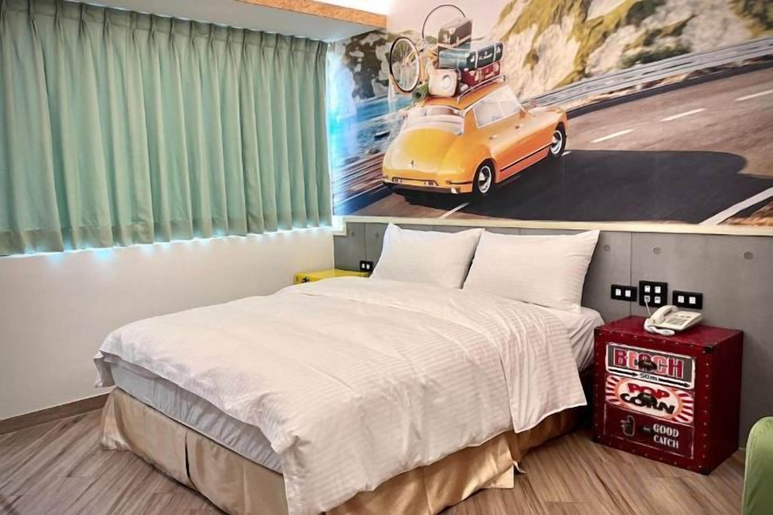 A bed with a white comforter, a headboard with a phone, and a wall with a road and car mural.