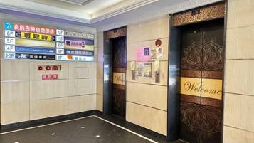 An elevator interior with a digital directory sign, a welcome sign, and a door with a decorative pattern.