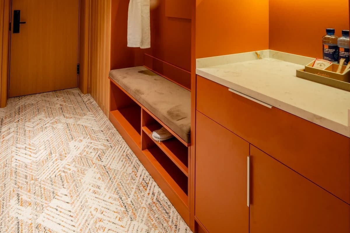 Habitación de hotel con un armario de madera, un banco, una bata, un lavamanos y una planta pequeña.