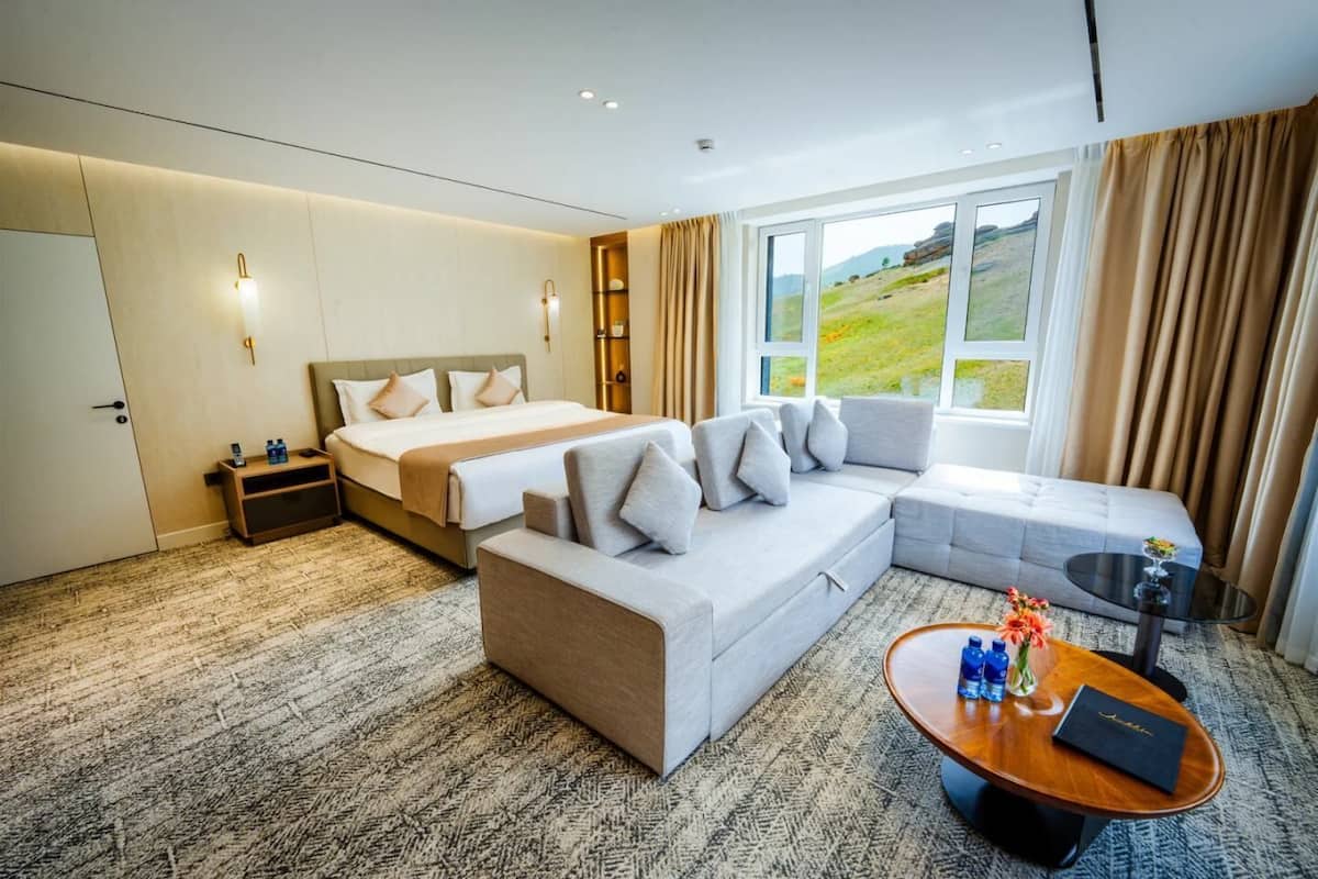 Una habitación de hotel con cama, sofá y una pequeña mesa con un florero y un libro.