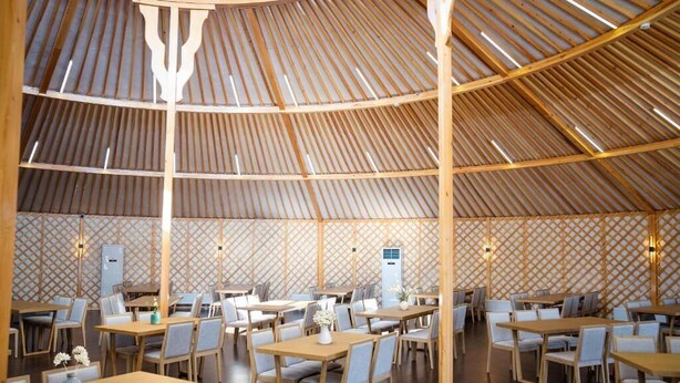 A spacious restaurant with a high, sloped ceiling and a patterned wall design. Tables and chairs are arranged for dining. - Juulchin Terelj Resort (Ulaanbaatar)