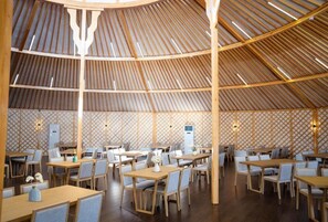 A spacious restaurant with a high, sloped ceiling and a patterned wall design. Tables and chairs are arranged for dining. - Juulchin Terelj Resort (Ulaanbaatar)