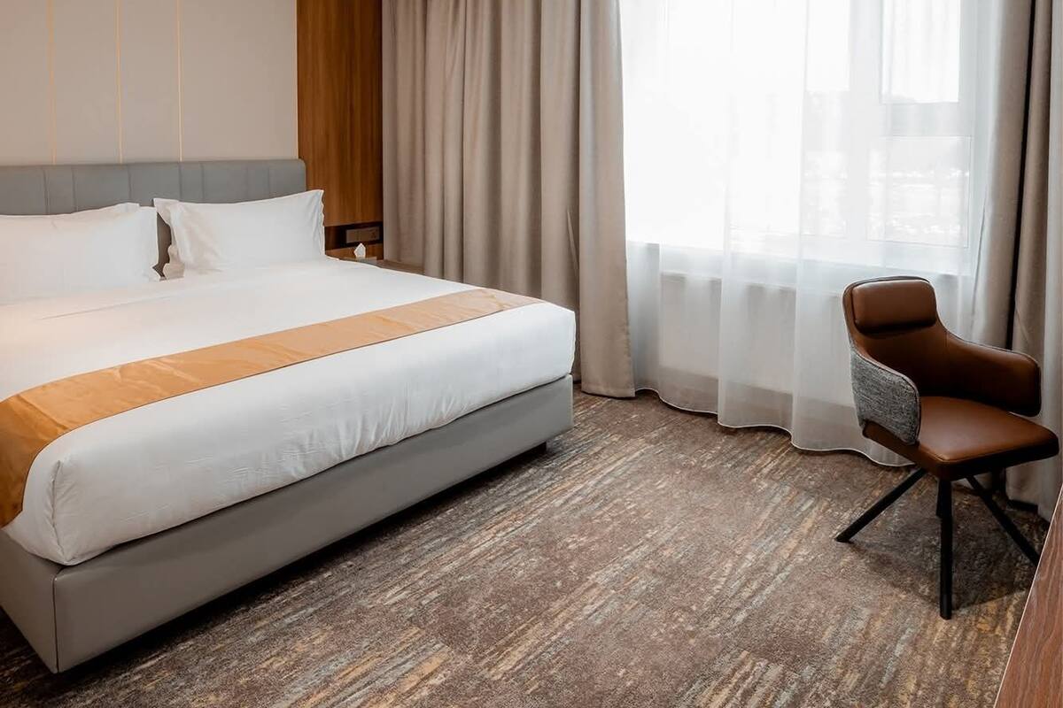 Una habitación de hotel con una cama grande, una silla y una ventana con cortinas.