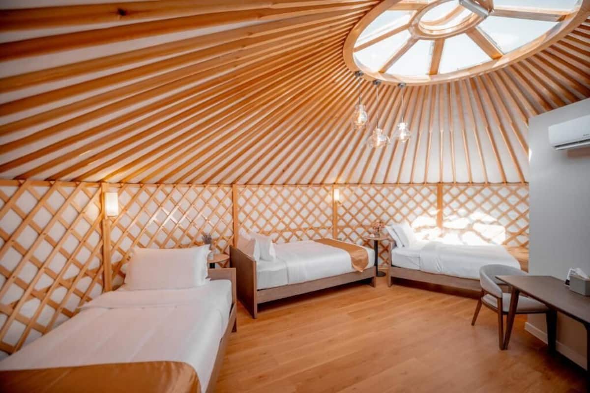 Una habitación estilo yurta con dos camas, un escritorio y una claraboya circular.