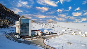 A modern building with a glass facade, surrounded by a snowy landscape with small houses and storage tanks. - Juulchin Terelj Resort (Ulaanbaatar)