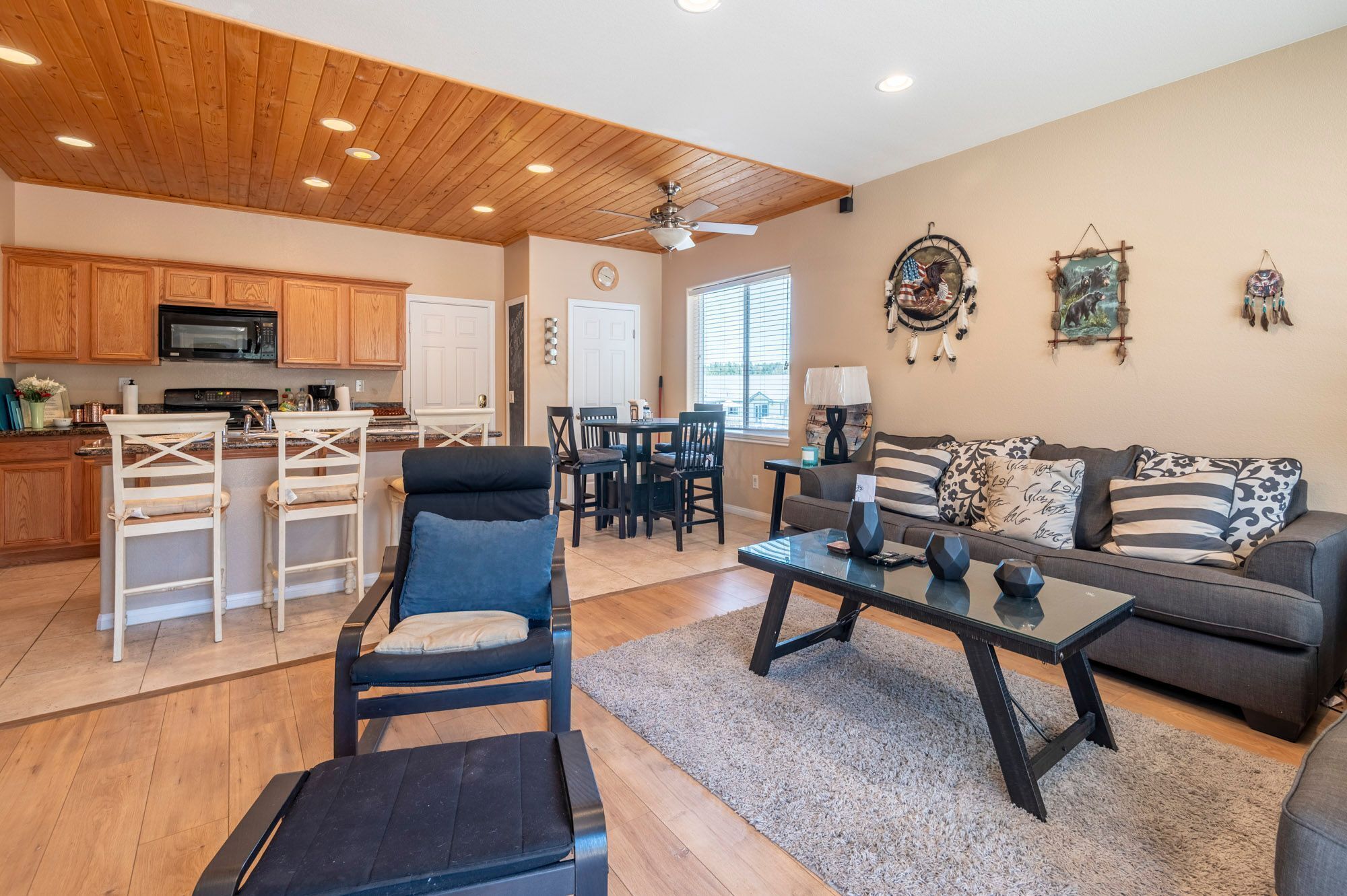 A modern living room with a wooden ceiling, a dining area, and a kitchen with wooden cabinets.