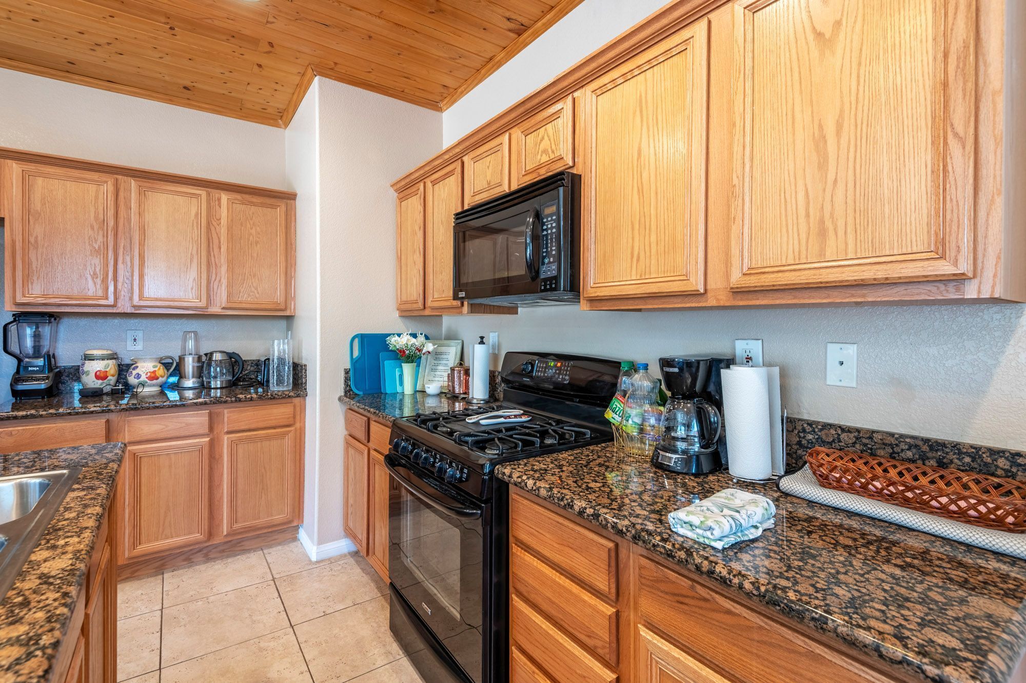 A kitchen with wooden cabinets, a microwave, stove, granite countertops, and various kitchen appliances.