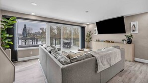 A modern living room with a grey sofa, a coffee table, and a large window overlooking a balcony. - Portage Lakes Retreat with Boat & Views (New Franklin)
