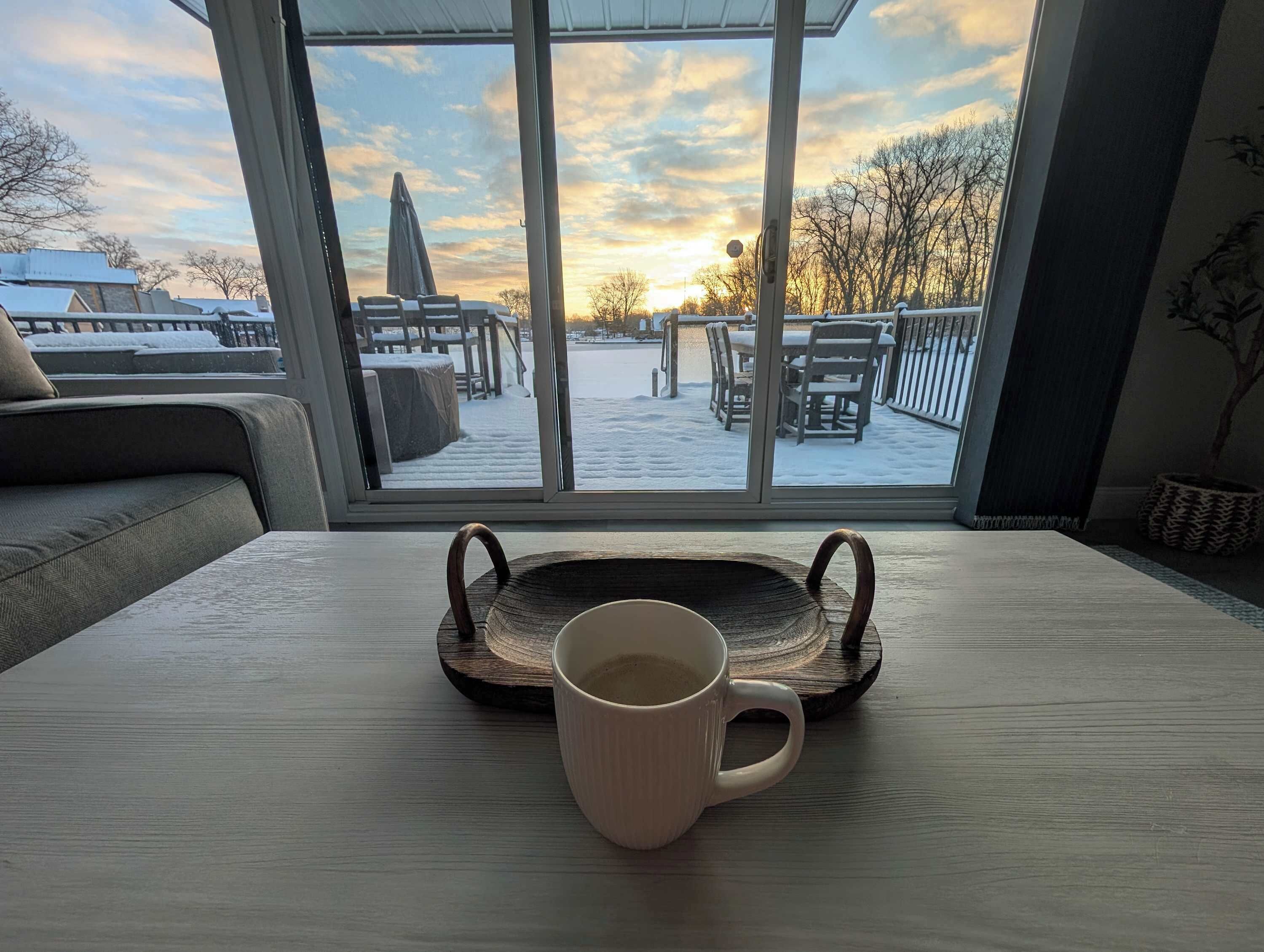A view from a window overlooking a snowy outdoor deck with a table and a mug.. PLX Spring and Summer Getaways!  3BR Lakefront Sleeps 8