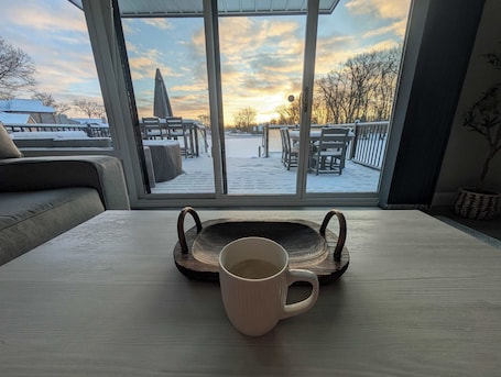 A view from a window overlooking a snowy outdoor deck with a table and a mug.. PLX Spring and Summer Getaways! 3BR Lakefront Sleeps 8