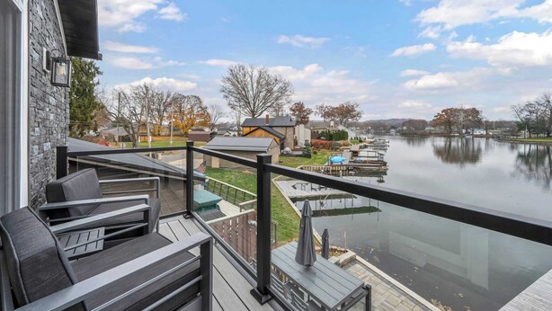 A deck with outdoor furniture overlooking a calm lake, surrounded by residential buildings and trees. - Portage Lakes Retreat with Boat & Views (New Franklin)