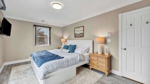 A bedroom with a bed, bedside tables, a nightstand, a window, and a door. - Portage Lakes Retreat with Boat & Views (New Franklin)