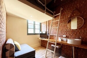 Una habitación compacta con pared de ladrillo, suelo de madera, sofá, escalera, lavabo y espejo.