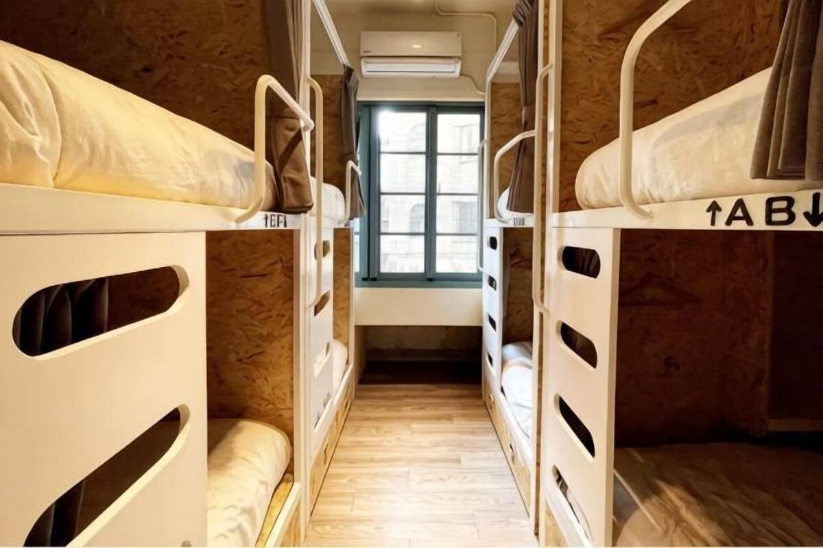 Un couloir étroit avec des lits superposés, une fenêtre et un appareil de climatisation.