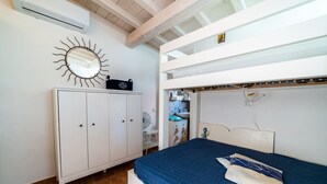 Une chambre avec un lit superposé, une armoire, un miroir au motif rappelant le soleil et une petite icône religieuse accrochée au mur.