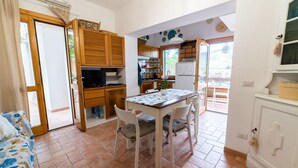 Une cuisine compacte avec des meubles en bois, une table à manger avec des chaises et une vue sur l’extérieur grâce à une porte vitrée.