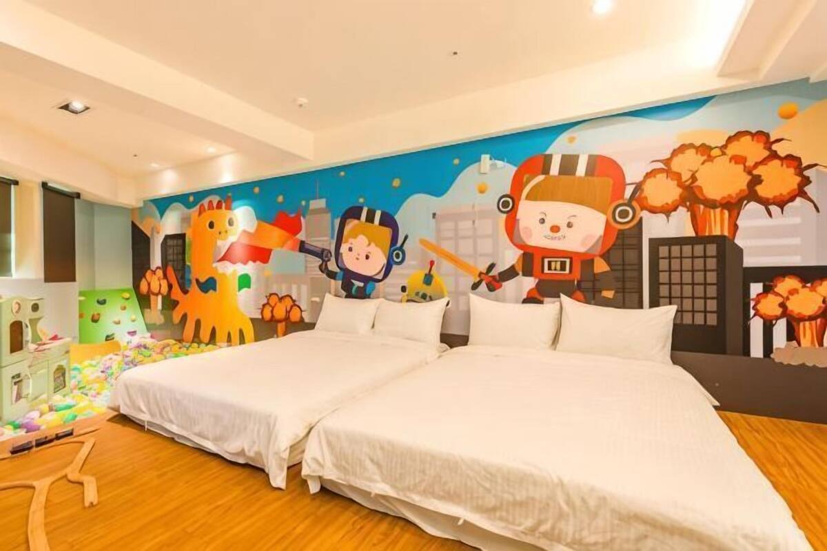 A hotel room with two beds, a mural with cartoon characters, and a play area with toys.
