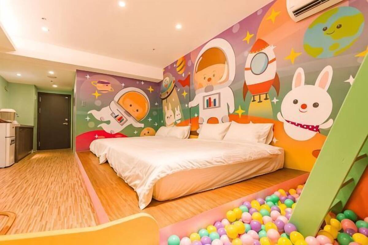 A bedroom with a bed, a wall mural, a ball pit, and a small desk.