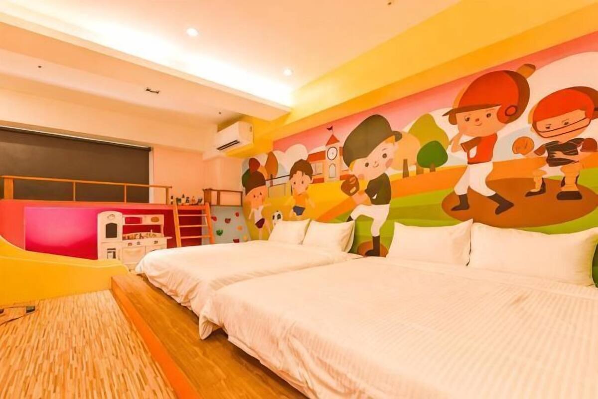 A hotel room with two beds, a large mural on the wall, a desk, and a window.