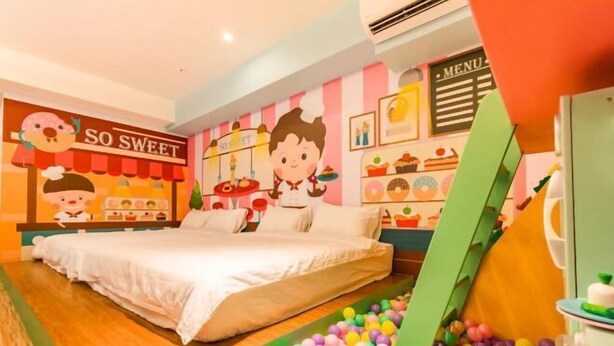 A brightly colored children's room with a bed, a ball pit, and a wall decorated with cartoon characters and food items. - Kids Fun Hotel (Yilan)