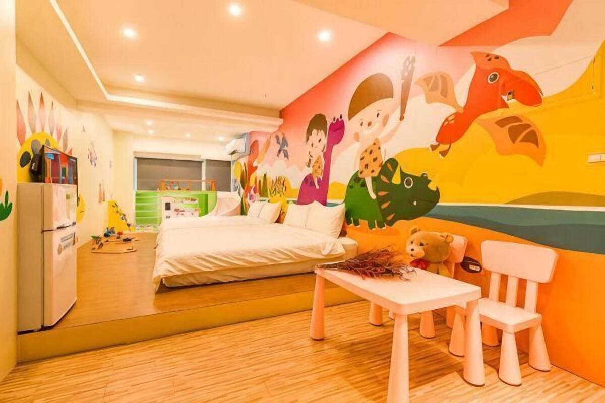 A child-friendly room with a bed, a table, chairs, and a mural.