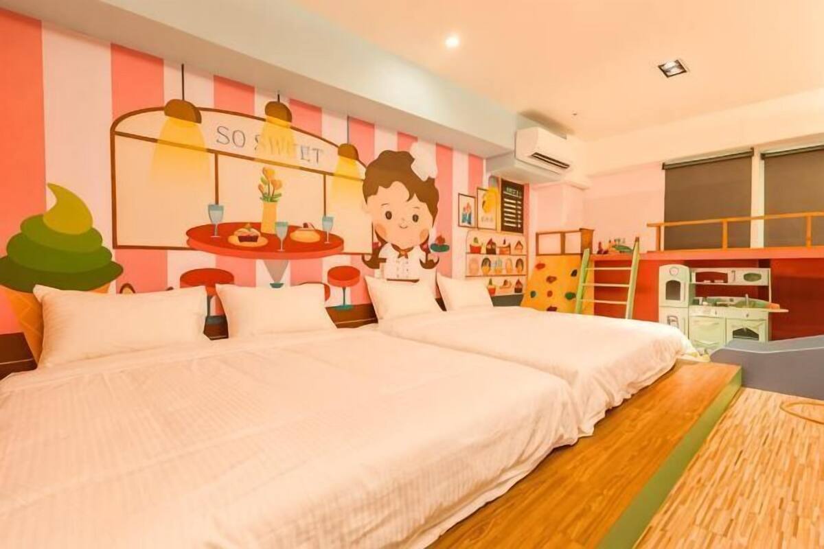 A hotel room with two beds, a kitchenette, a play area, and a large window.