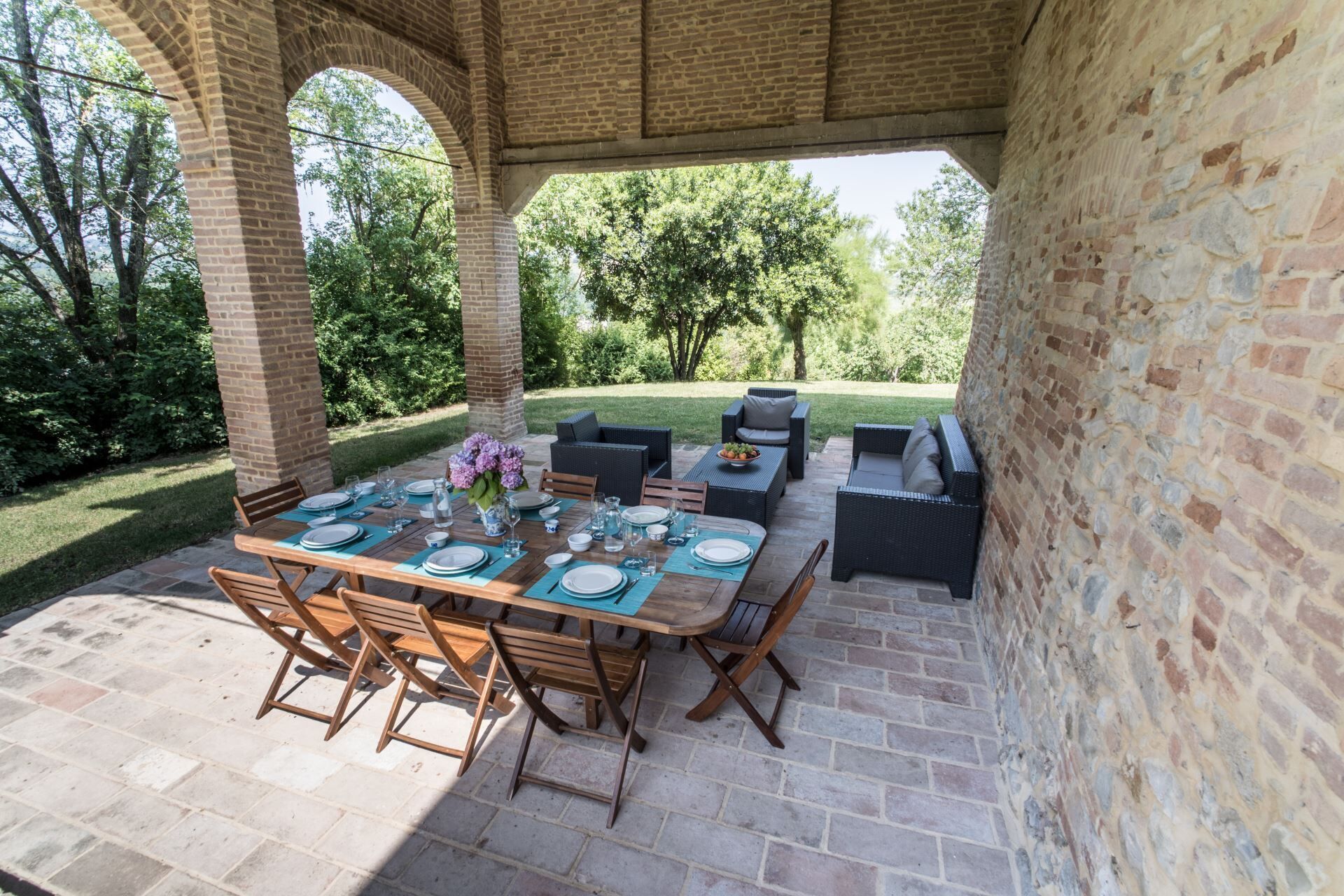 Un patio al aire libre con un arco de ladrillo, una mesa de madera dispuesta para comer y asientos exteriores.