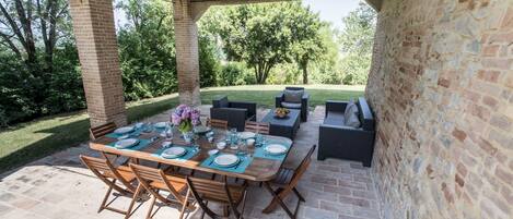 Un patio al aire libre con un arco de ladrillo, una mesa de madera dispuesta para comer y asientos exteriores.