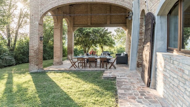 An outdoor patio with a brick archway, a dining table set for four, and a view of the surrounding greenery.