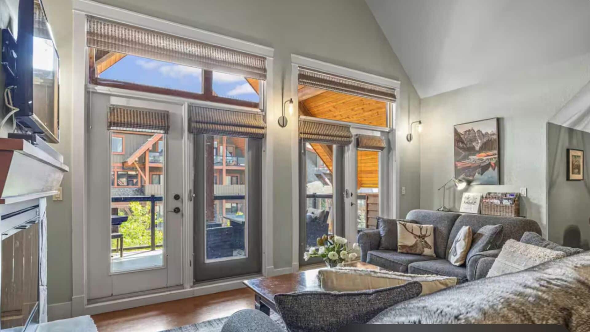 A spacious living room with a large sofa, a coffee table, and a fireplace. There are large sliding glass doors leading to an outdoor area with a view of buildings.