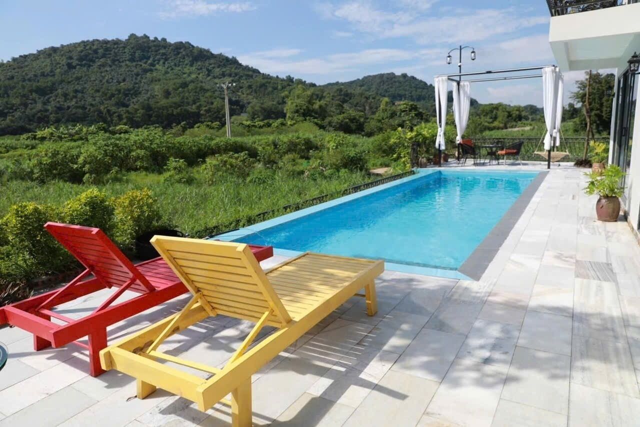 Une piscine avec deux chaises longues, une rouge et une jaune, et un bâtiment blanc doté d’un balcon.