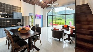 A modern kitchen with a dining area, a large window offering a view of greenery, and a wooden staircase. - Le Soleil Ba vi (Hanoi)