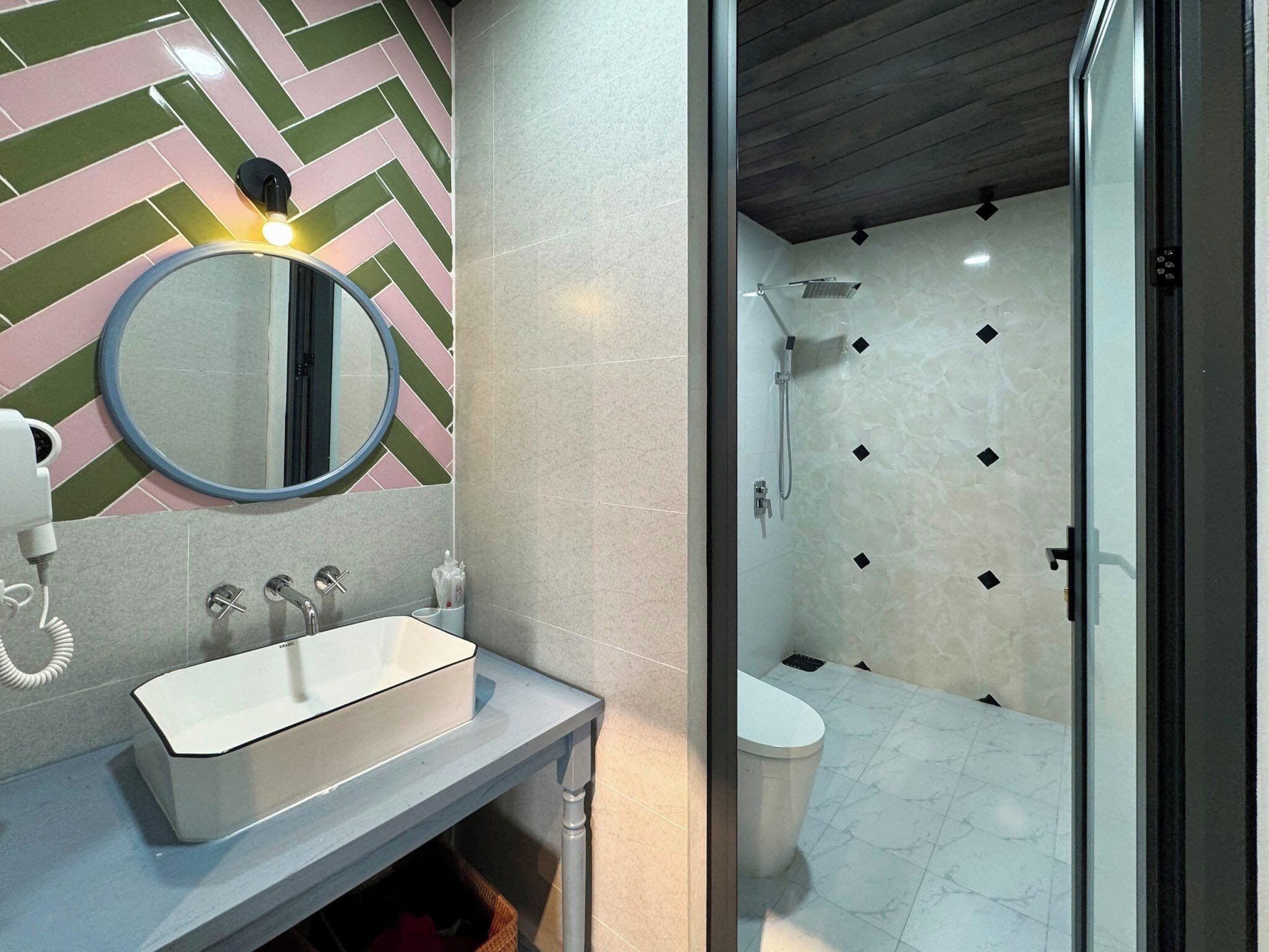 A modern bathroom with a herringbone-patterned wall, a round mirror, a white sink, and a shower area with a tiled floor.