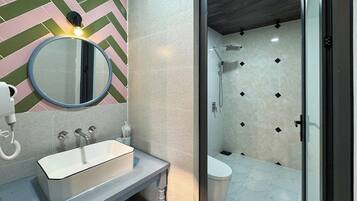 A modern bathroom with a herringbone-patterned wall, a round mirror, a white sink, and a shower area with a tiled floor.