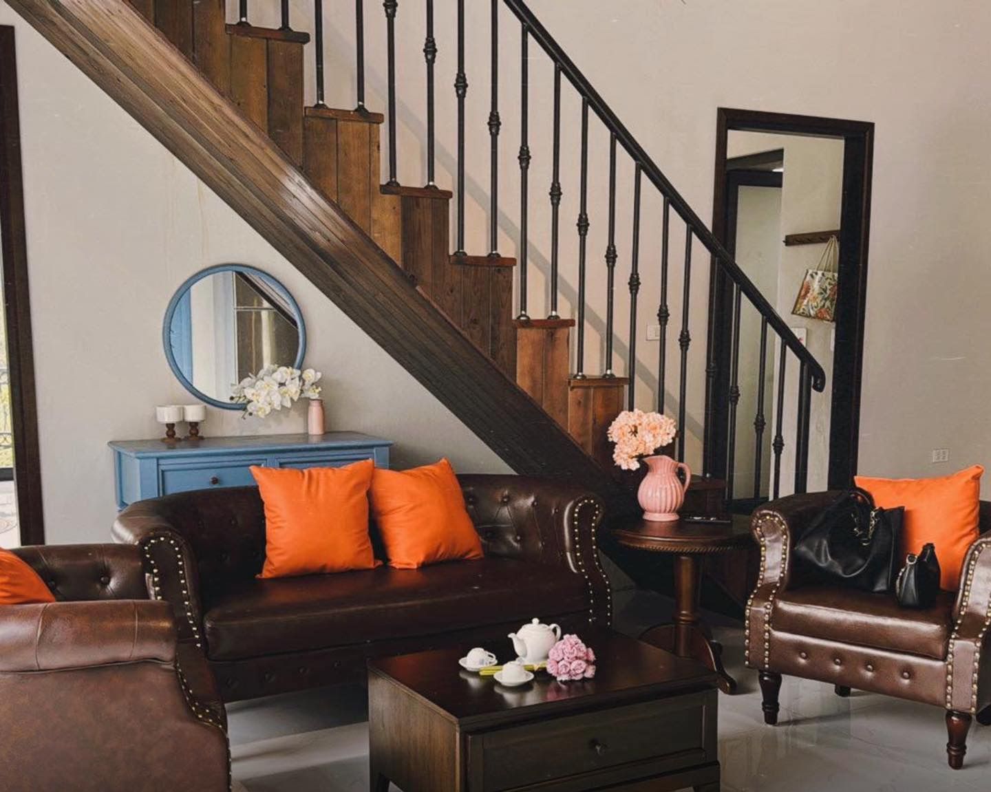 Un salon avec un escalier, une commode bleue et une table basse ornée de fleurs.