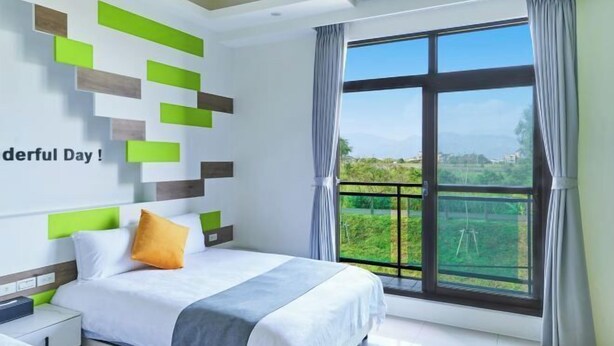 Una habitación de hotel con cama, mesita de noche, ventana que ofrece vistas a zonas verdes y pared con diseños geométricos.