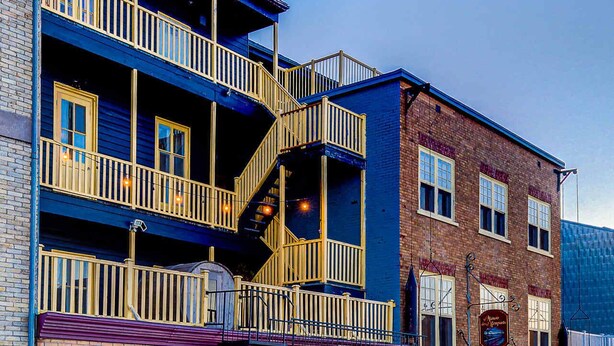 A multi-story hotel with a blue facade, a ground-level entrance, and a balcony with yellow railings. - Double room river view (Québec)